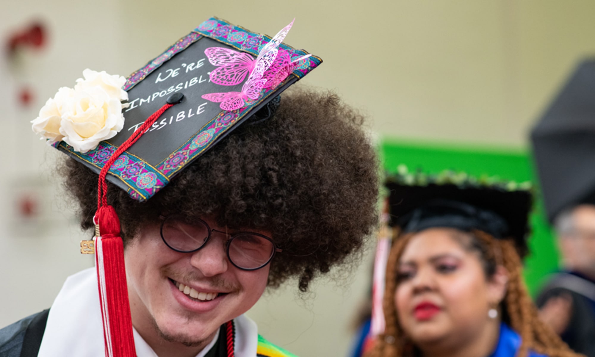Student graduation cap decorated with butterflies and roses that reads 'we're impossible impossible'