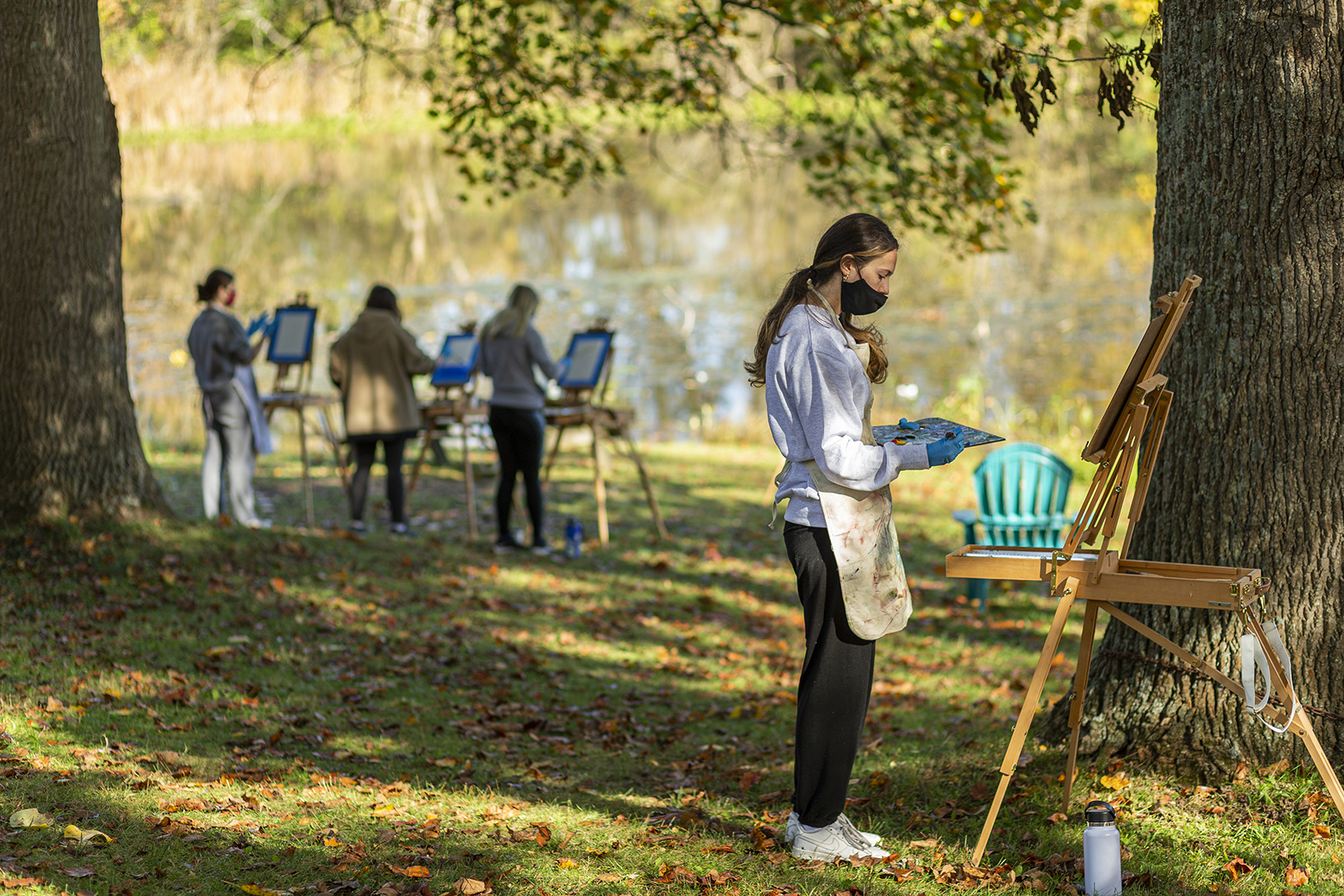Students paint on easels outdoors while wearing masks